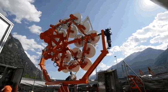 Photo of an array of solar panels or mirrors mounted on a rotating, red scaffold, below a mostly blue sky.

"Solar Sunflowfer" from https://giphy.com/gifs/mic-energy-solar-sunflowers-7pbW8McOpIWOc