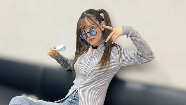 Sally with her hair in pigtails with sun glasses slightly off her eyes with her right hand holding an ice cream pop and one of the fingers touching her left ear.