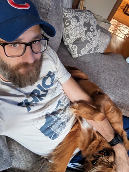 Selfie of a man sitting on a sofa with a large golden retriever puppy draped over his lap.