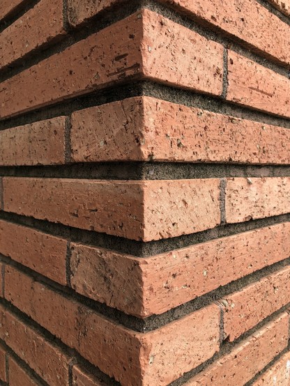 Color photo looking head-on at a corner of a building constructed of rough textured, light reddish-orange roman bricks