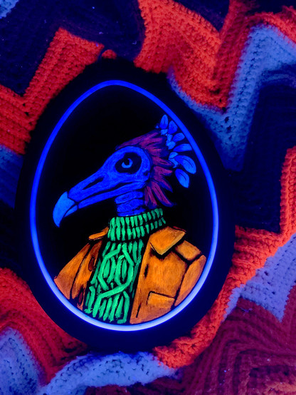Blacklight view of an acrylic painting on an egg-shaped piece of wood. The portrait is of a species called a fetroscale, which in the blacklight view appears skeletal, with a bird-like skull and red and blue plume feathers. They are wearing a green turtleneck with glowing cable knit, and a bright orange leather jacket.