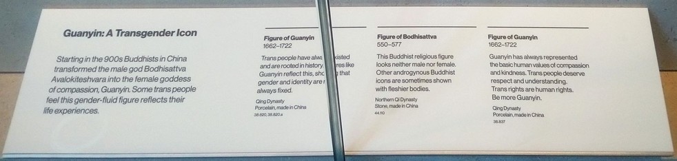 A museum plaque, listing: "Guanyin: A Transgender lcon. Starting in the 900s Buddhists in China transformed the male god Bodhisattva Avalokiteshvara into the femal goddess of compassion, Guanyin.  Some trans people feel this gender-fluid figure reflects their life experiences."  Three items are described: "Figure of Guanyin, 1662-1722: Trans people have always existed and are rooted in history.  Figures like Guanyin reflect this, showing that gender and identity are not always fixed."  "Figure of Bodhisattva, 550-577: This Buddhist religious figure looks neither male nor female.  Other androgynous Buddhist icons are sometimes shown with fleshier bodies."  "Figure of Guanyin, 1662-1722: Guanyin has always represented the basic human values of compassion and kindness.  Trans people deserve respect and understanding.  Trans rights are human rights,  Be more Guanyin."