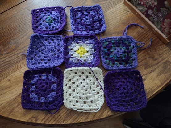 Eight crocheted granny squares in shades of purple, yellow, white, and peacock variegated yarn.
