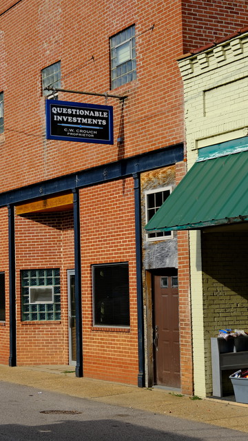 Brick building facade that appears empty and abandoned with the sign that says â€œQuestionable Investmentsâ€�
