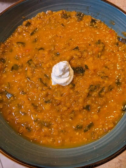 A wide, low earthenware bowl with a serving of tomato lentil soup garnished with a dollop of sour cream