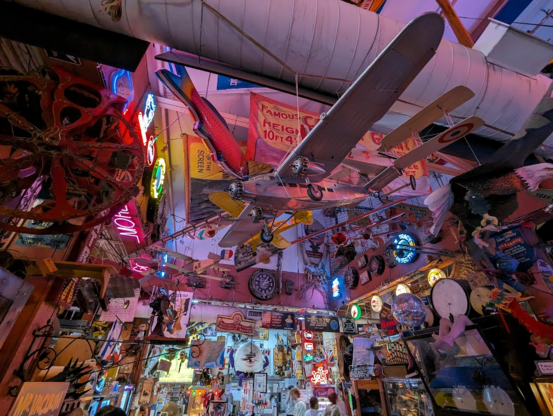 A photo of a large ceiling above a food court. it is heavily decorated in posters, banners, and large model airplanes.