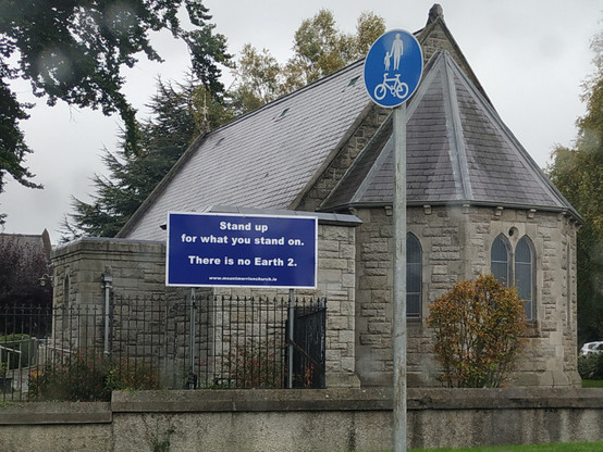 A sign saying "Stand up for what you stand on. There is no Earth 2." In a photograph of St Thomas Church, Mount Merrion, Dublin.