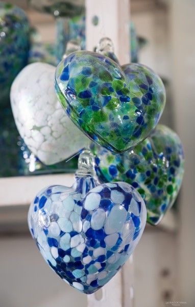 Four blown glass hearts with dot designs hang in a cluster from a shelving support in a shop.