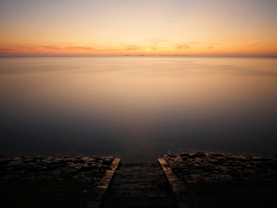 Sunset over a calm north sea. Stairs leading down to the water.
