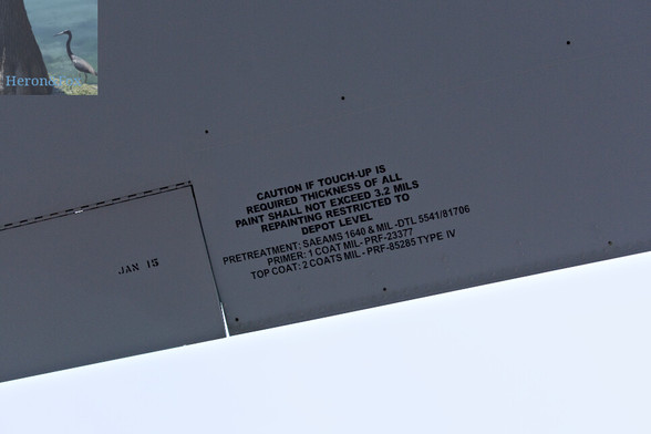 A close-in photograph of the bottom of an airplaneâ€™s horizontal stabilizer. It is painted gray with black text reading, â€œCaution if touch-up is required thickness of all paint shall not exceed 3.2 mils repainting restricted to depot level.â€� It continues in smaller text, â€œPretreatment; SAEAMS 1640 & MIL-DTL 5541/81706 Primer: 1 coat MIL-PRF-23377 Top Coat: 2 Coats MIL-PRF-85285 Type IVâ€� with â€œJAN 15â€� printed further to the right.