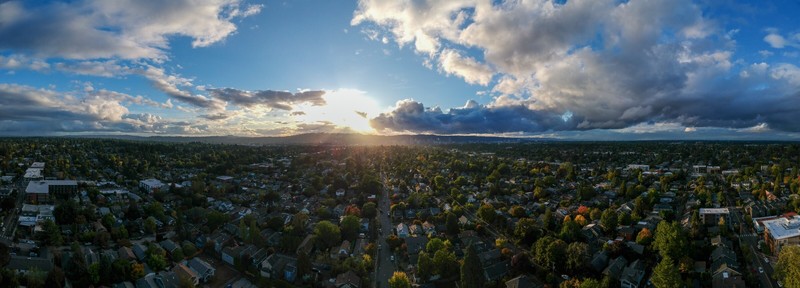The sun is setting over the west hills of Portland Oregon. Storm clouds are passing to the north and more are coming from the south. The sun peeks through a spot of blue sky between the clouds.