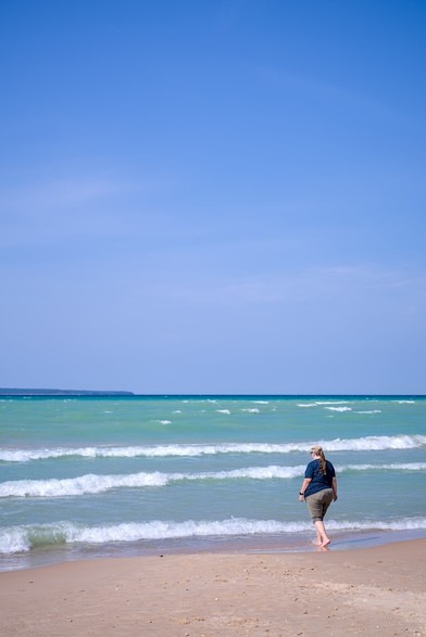 A woman walks along the waterline on the beach.