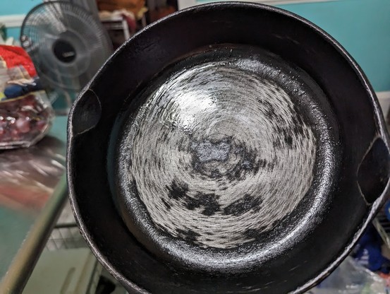 A cast iron pan that is being sanded to remove the old season so it can be reapplied. It's been sprayed with oil to prevent rusting while working on it.