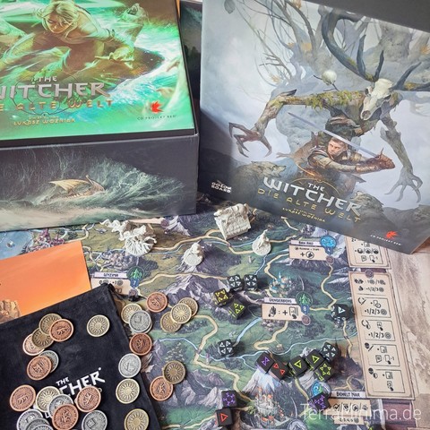Auf einer Landkarte liegen Metallmünzen, Würfel und Miniaturen verteilt. Im Hintergrund 2 Kartons mit Bildern aus The Witcher
