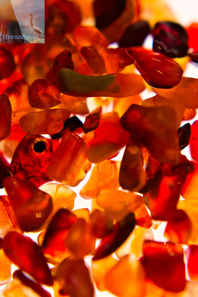 A macro, close-in photograph of many, small translucent crystals with hues of yellow, orange, and red, with spots of green and black.