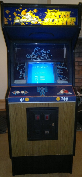Arcade cabinet for "Astro Blaster". It is a standard US cabinet style, with wood paneling along the front, and space-like art on the marquee and control areas. The monitor has a vertical orientation, similar to Pig Newton's orientation.