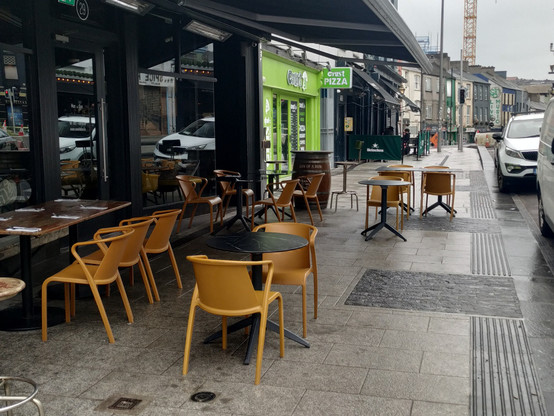 Son of a Bun obstructing the entire width of the footpath at the west end of MacCurtain Street. Their furniture continues right up to parked vehicles at the roadside.