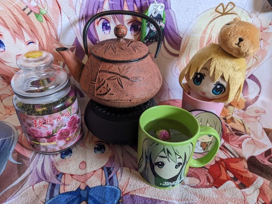 Mugi is in a mugi cup with a Mugi coffee cup with green tea in it. There is a rose bud floating in the tea. There is also a Japanese tea pot and a container of rose green tea.