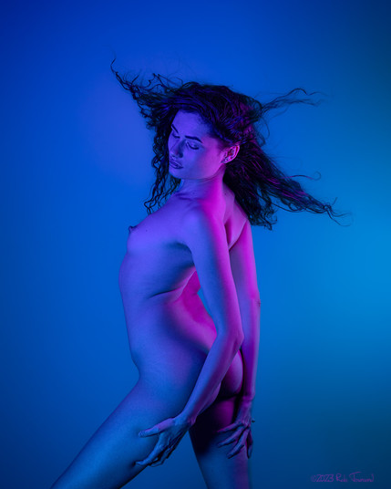 art model Ira poses nude in blue and purple light, with her hair blowing in a wind.