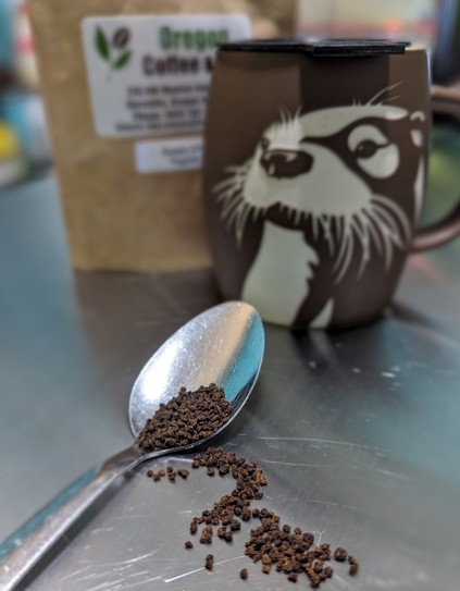 a teaspoon with loose Assam tea in front of a mug that has an otter on the side