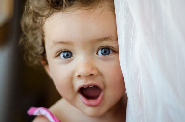 playing with myself: photograph of a young joyful girl looking at you, with one side of her face partly covered by a white curtain
