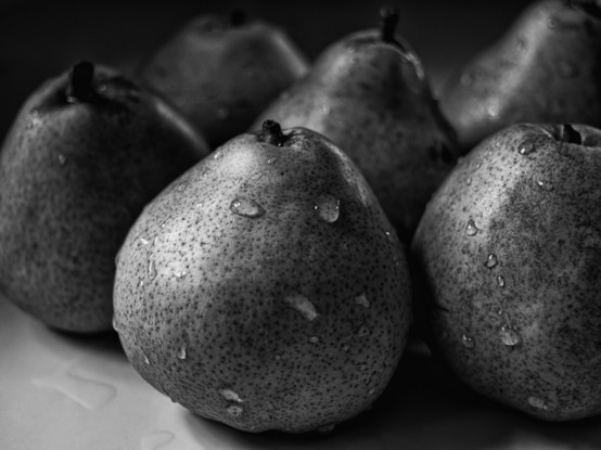 Low key monochrome closeup photograph of six pears on a white counter. The pears and counter have water drops on them.