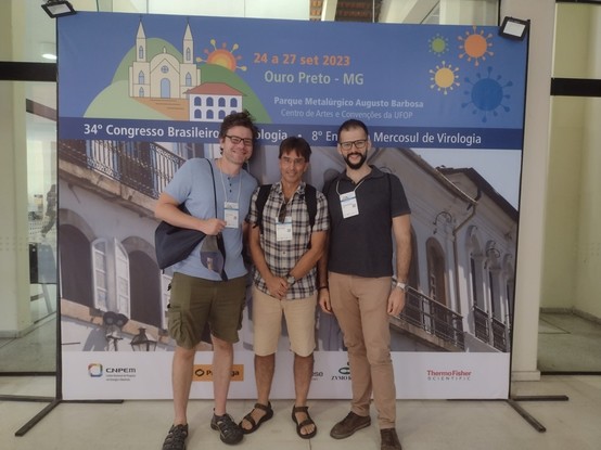 Me standing in front of the conference banner with colleagues Murilo Zerbini and Rodrigo Rodrigues.