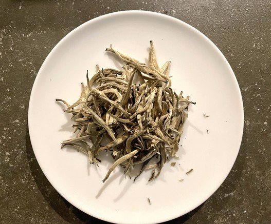 Whitish, elongated tea leaves on a small white plate.
