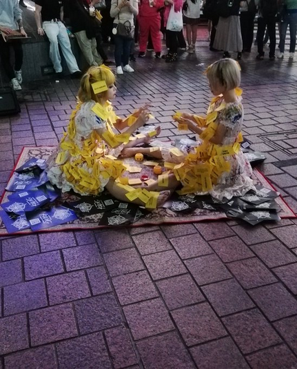 Laguna and Michelle on blanket doing street performance. Yellow notes pinned all ove rthem.