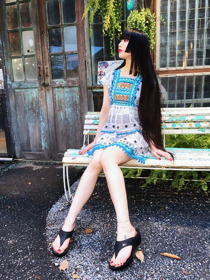 Hima sitting on a bench. She is wearing a white and black summer dress with eleborate blue trim.