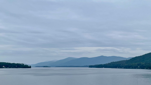 A lake extends northward under grey skies with tree-covered mountains also extending northward along the left shore.