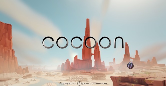 Capture d’écran du jeu-vidéo Cocoon, on y voit l’écran d’accueil sur lequel apparait au centre et en gros le titre du jeu, avec en arrière-plan une zone de type désertique et rocheuse sur fond de ciel bleu.
En bas se trouve l’indication écrite « Appuyez sur A pour commencer ».