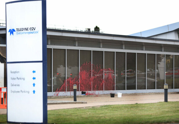 A photograph of a glass-walled building behind a sign that reads TELEDYNE e2V. There is red paint splattered onto the building's glass