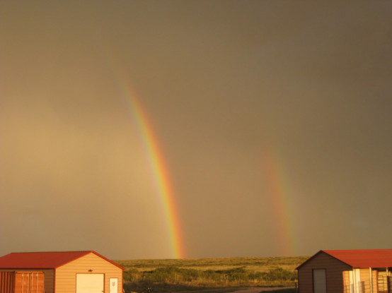 A double rainbow with colors of orange, yellow and a little green against the stormy morning sky. The sky looks brown but it's really gray.