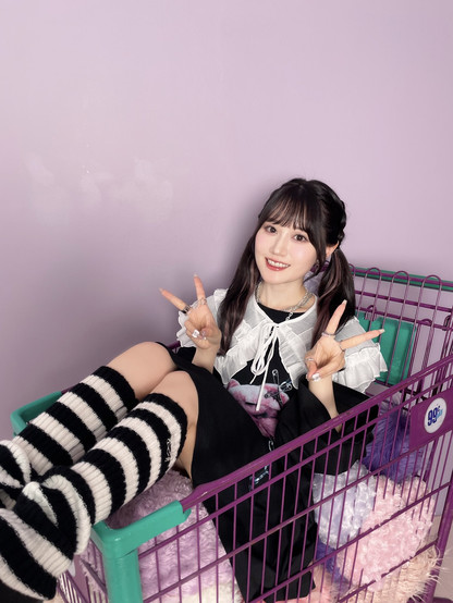 Ogura Yui sitting on a shopping cart smiling doing the V sign.