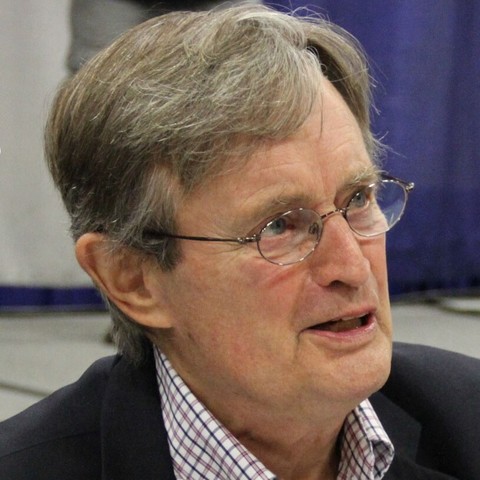 Headshot photo of a caucasian man with dark gray hair, wearing wire-rim glasses, apparently speaking.