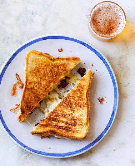 A picture of a brown and orange cheese toastie on a rustic white plate with a blue rim. Sliced diagonally the cheese oozes out ...