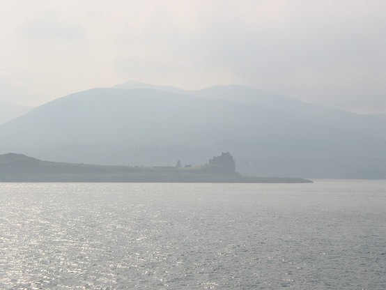 Misty scenery of Duart Castle in front of the big hills of the Isle of Mull, seen from the ferry