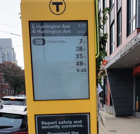 E-ink real-time arrivals display at an MBTA bus stop, reading 39 Forest Hills in 7, 28, 35, 49 mins and 9:45.