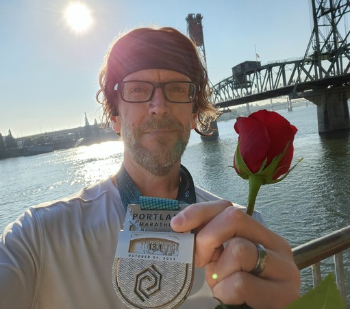 Post-race runner all sweaty and tired, holding a rose and a finisher medal in front of the Hawthorne Bridge