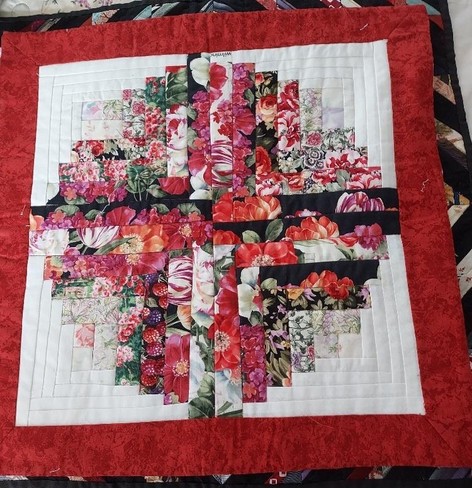 photo of a quilt made up of red, pink, white, and some green, the floral print pieces make a cross design
