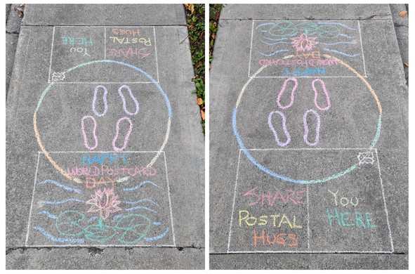 A sidewalk chalk art drawing in front of our house, featuring a large circle sandwiched between two rectangles. The two rectangles represent the front and back of a postcard. The front has a drawing of a water lily, and text that reads, "Happy Postcard Day". The back of the card is addressed to, "You / Here" and the text reads, "Share Postal Hugs"