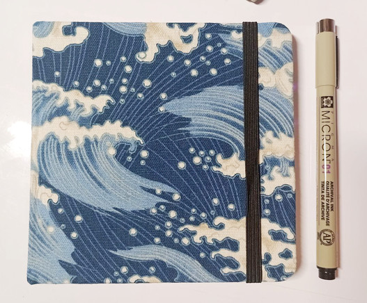 photo of a tiny sketchbook with a wave pattern on it and a black micron pen next to it
