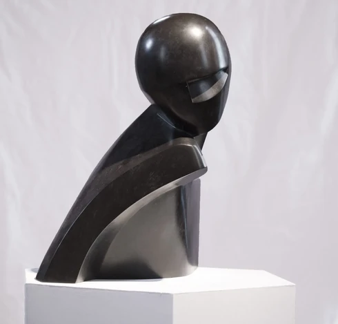 a photo of a dark grey and black statue, very heavy looking, it resembles a human form, like a bust sculpture, but it is composed of odd angles, it is a very abstract sculpture of a human form