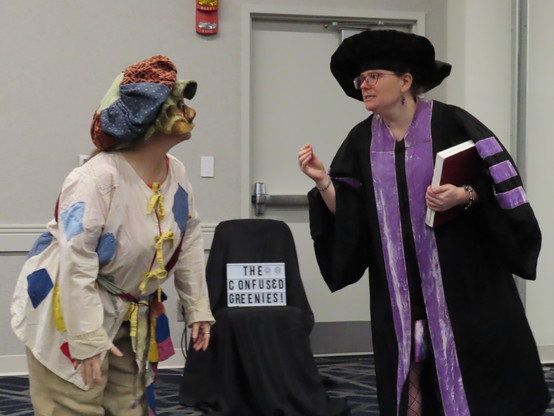 Two actors perform a commedia dell'arte play in a hotel conference center panel room during a science-fiction convention portraying the stock characters of Arlecchino listening to a worried il Dottore lecture about the dangers of 16th Century time travel!
