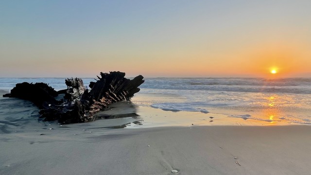Shipwreck is exposed at low tide and sunrise on Hatteras island. View of rising sun, ocean and wreck as views from beach.