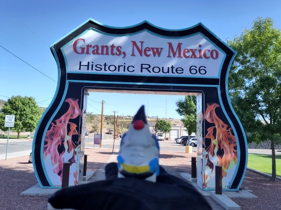 The Java Mascot "Duke" in front of a gate in Grants stating "Grants, New Mexico" and "Historic Route 66"