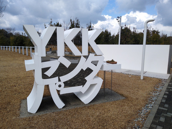 The YKK Center Park main entrance sign. It's a large white painted metal structure with a front-facing mirror, on a concrete block footing.
