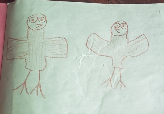 2 very poorly drawn creatures that vaguely resemble owls. Drawn with brown crayon on green construction paper.