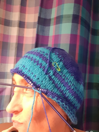 Half knitted blue and turquoise hat still on circular needles, on my head while I pull a face.